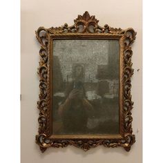 an ornate gold framed mirror hanging on the wall next to a white wall with a reflection of a man taking a selfie