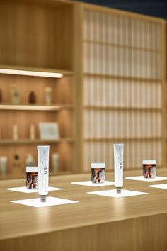 four tubes are lined up on a table in front of shelves with books and vases