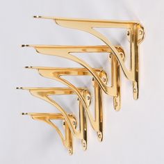 a set of five gold - plated hooks hang on the wall, each holding several pairs of scissors