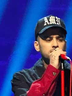 a man holding a microphone up to his mouth while wearing a hat and red shirt