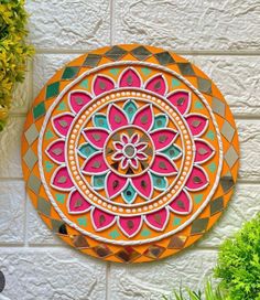 an orange and pink wall hanging on the side of a white brick building with potted plants