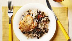 a white plate topped with rice and beans next to a yellow fork on top of a table