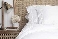 a bed with white sheets and pillows next to a lamp on the side table in front of it