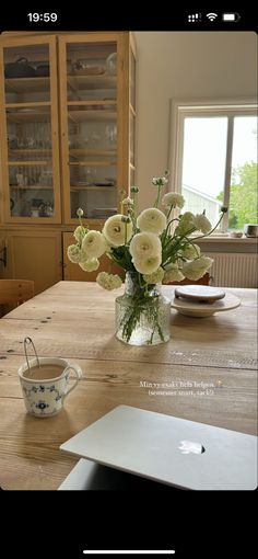 a vase filled with white flowers sitting on top of a wooden table next to a laptop computer