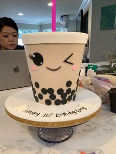 a birthday cake sitting on top of a table next to a laptop computer and a woman