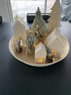 a white plate topped with small houses and christmas trees on top of a table next to a window