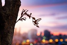 the silhouette of two hummingbirds on a tree branch in front of a cityscape