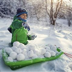 a little boy playing in the snow with some balls