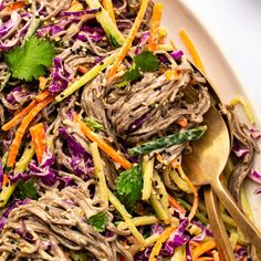 a white plate topped with shredded meat and veggies next to a gold spoon