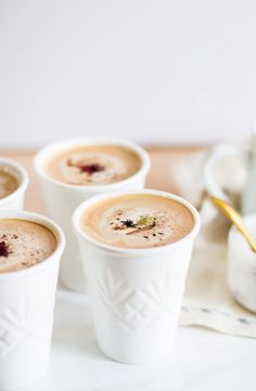 four cups filled with liquid sitting on top of a white table next to a gold spoon