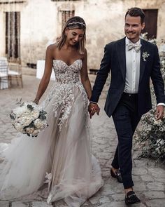 a bride and groom walking down the street holding hands in front of an old building