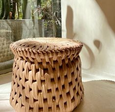 a wicker stool sitting on top of a floor next to a potted plant