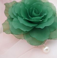 a large green flower on top of a white table cloth with a pearl brooch