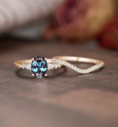 two gold rings with blue and white stones on them sitting on a wooden table next to a rose