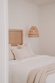 a bed with white linens and pillows in a room that has light colored walls