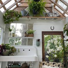 a white sink sitting under a wooden roof in a room filled with potted plants