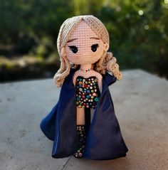 a crocheted doll dressed in a blue cape and holding a beaded umbrella