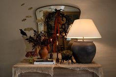 a table with two vases, a lamp and a book on it in front of a mirror