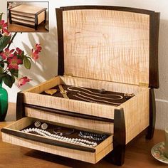 an open wooden box on a table with flowers in the vase and other items around it