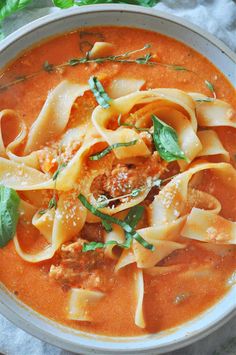 a bowl filled with pasta and sauce on top of a white cloth next to a green leafy garnish