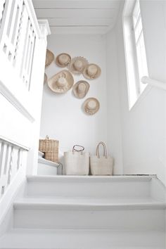 several hats are hanging on the wall above some white stairs with baskets and totes