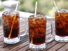 three mugs filled with iced tea sitting on top of a wooden table