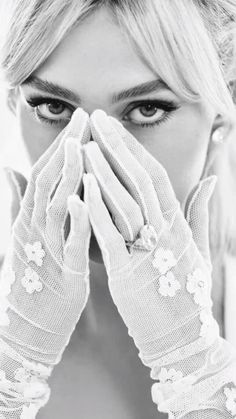 a woman wearing white gloves covering her face with her hands and looking at the camera