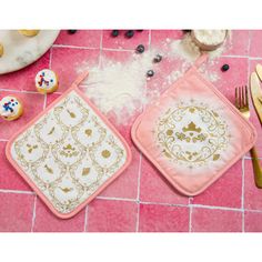 two pink and gold placemats sitting on top of a tile floor next to silverware