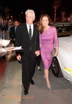 an older man and woman are walking down the street with their hands in each others'pockets