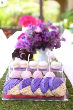 desserts are displayed on the grass in front of purple and pink flowers at an outdoor party