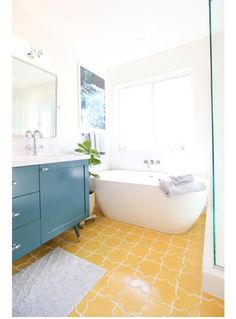 a bathroom with yellow and white tiles on the floor, blue cabinetry, and a bathtub