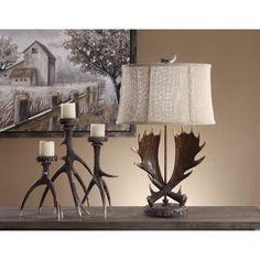 antlers and candles on a table in front of a painting with a barn scene