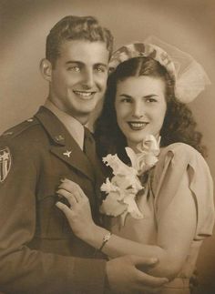 an old black and white photo of a man in uniform hugging a woman with flowers on her lap