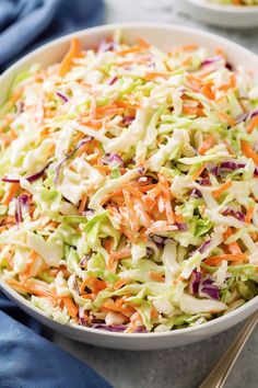 a white bowl filled with coleslaw and carrots next to a blue napkin