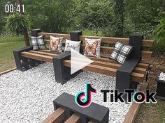 a wooden bench sitting in the middle of a gravel covered field with pillows on it