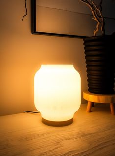 a white light sitting on top of a wooden table next to a potted plant