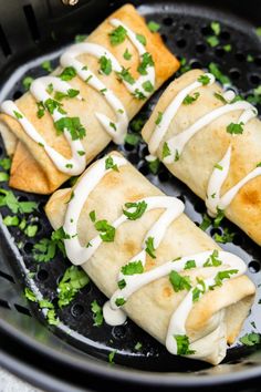 some taco shells are sitting in a frying pan with cilantro and sour cream drizzled on top