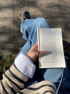 a person sitting on the ground holding an open book in their hand and listening to headphones