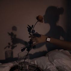 a person reaching for a rose in a glass on a bed with white sheets and pillows