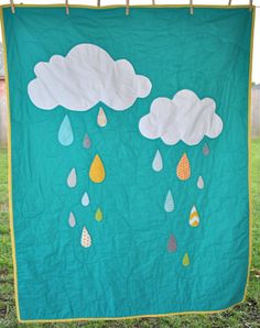 a quilt with rain and clouds on it hanging from a clothesline in the grass