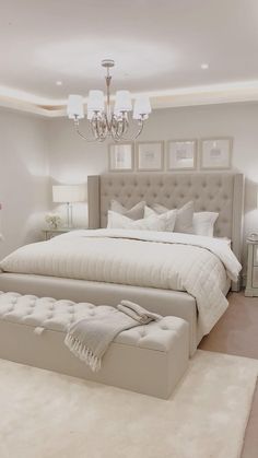 a large white bed sitting in a bedroom next to a chandelier and two lamps