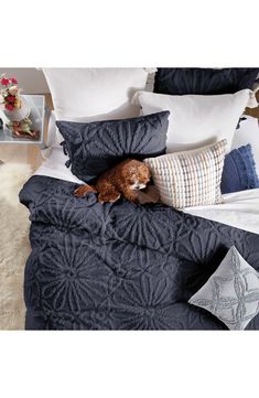 a dog laying on top of a bed covered in blue blankets and pillows with decorative throw pillows