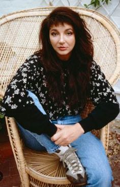 a woman sitting in a wicker chair with her hands on her knees and looking at the camera