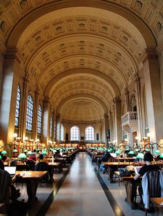 people are sitting at tables in the middle of a large room with high ceilings and arched windows