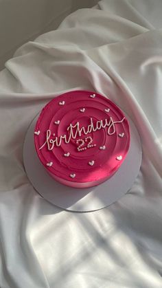 a pink birthday cake sitting on top of a white sheet