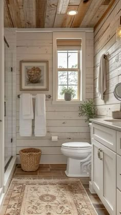 a white bathroom with wood paneling and a rug on the floor in front of the toilet