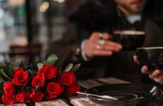 a bouquet of red roses sitting on top of a wooden table next to a black plate