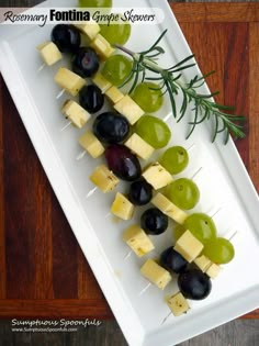 grapes and cheese skewers are arranged on a white plate with rosemary garnish