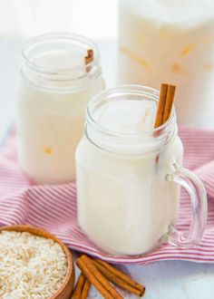 two mason jars filled with milk, cinnamon sticks and rice on a pink and white towel