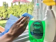 a hand holding a cloth near a bottle of detergent on a window sill